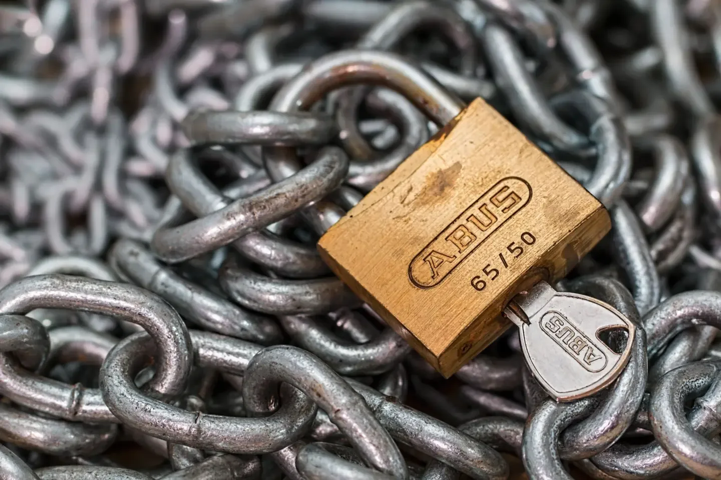 A brass padlock with its key lying on a pile of steel chains